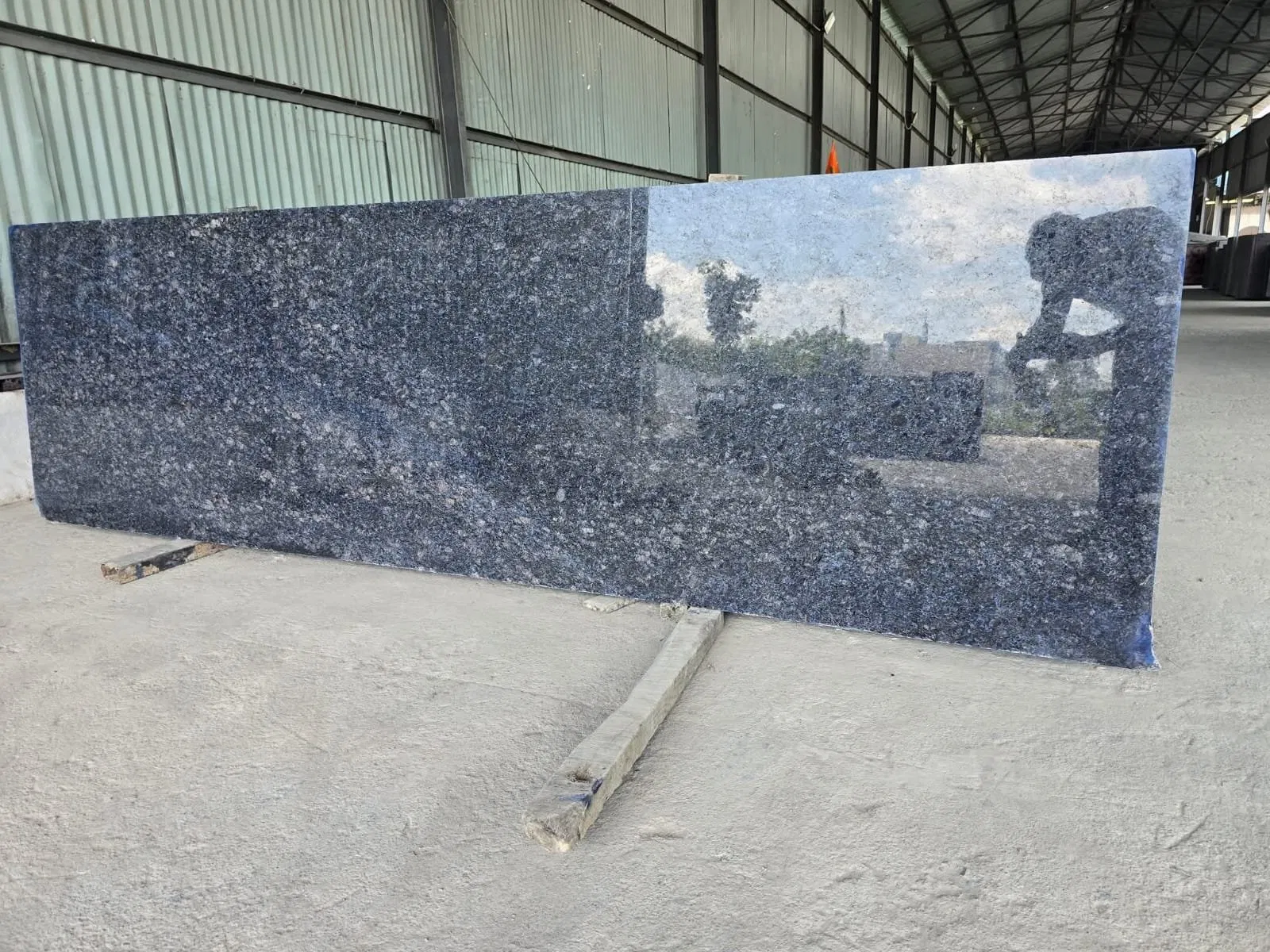 The Rarity of Lavender: An Insider's Look at South India's Most Unique Blue Granite 2 A display of Lavender Blue Granite slabs in a well-lit warehouse. One slab is polished to a high mirror-like gloss, while the adjacent slab has a matte leathered texture, demonstrating the visual versatility of the stone under different finishing processes.
