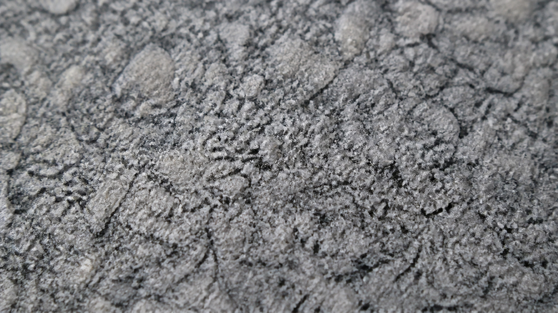 An extreme close-up of a flamed finish on grey granite, highlighting the slip-resistant texture required for safe public paving.